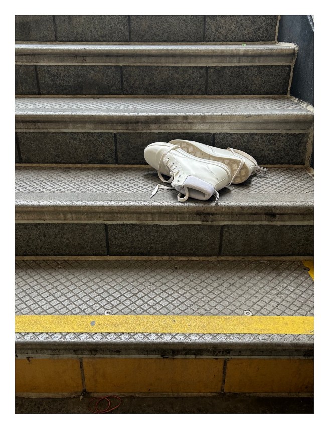clean white high-top shoes lie on their side on the grey gritty steps up from a subway platform