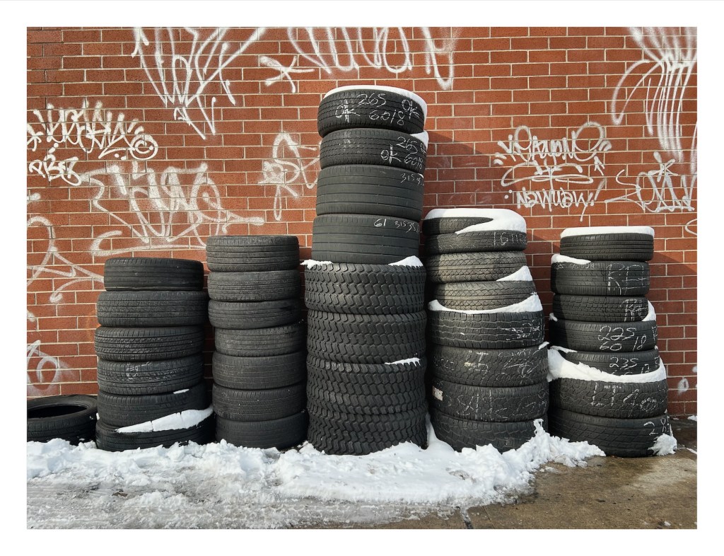 stacks of tires next to a brick wall, with snow piled on top and around them