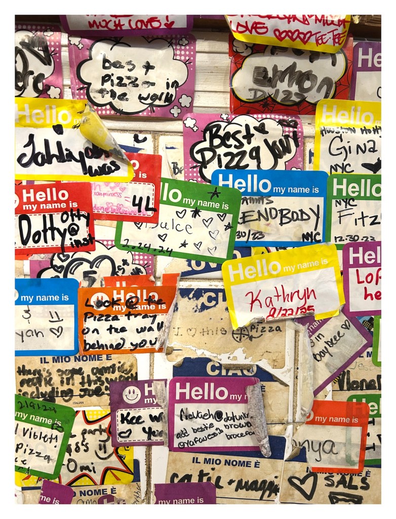 name tags stuck to a pizza shop wall, with writing that praising the food and staff