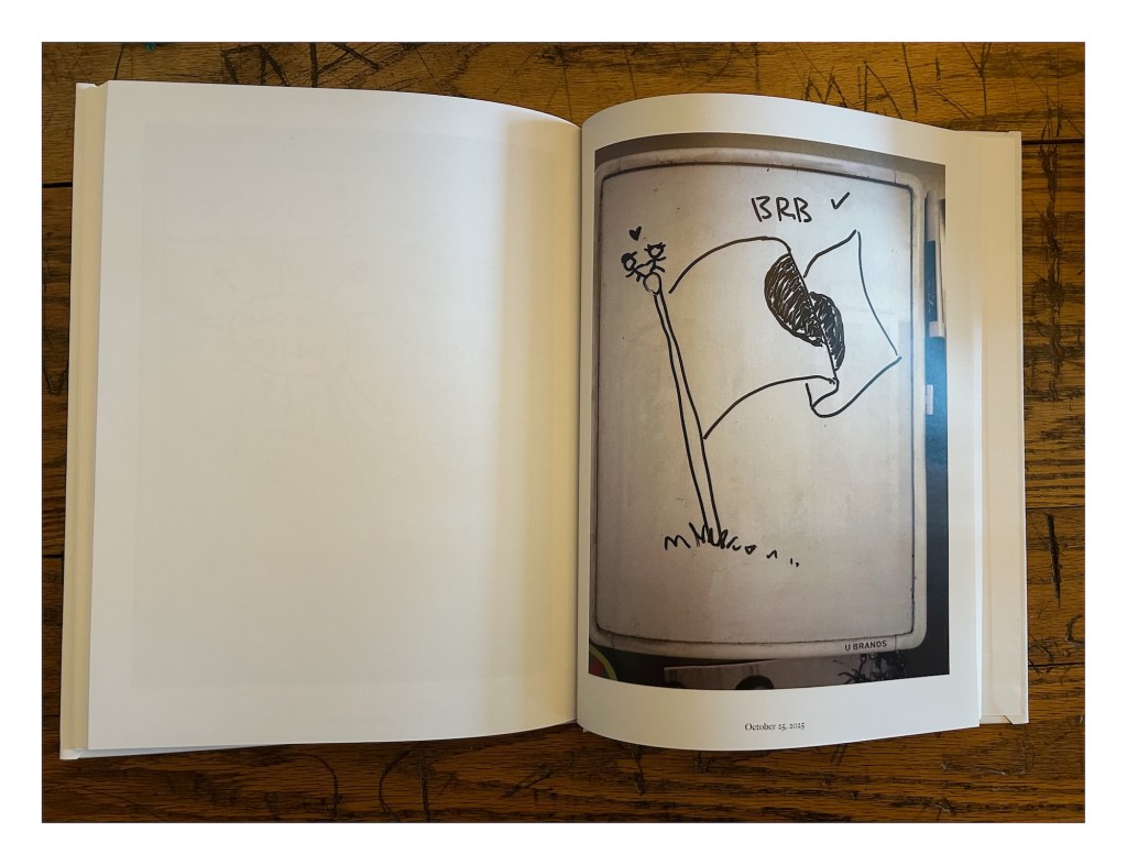 a photobook displays a drawing of the Japanese flag waving in the wind with two stick figures standing atop the flagpole