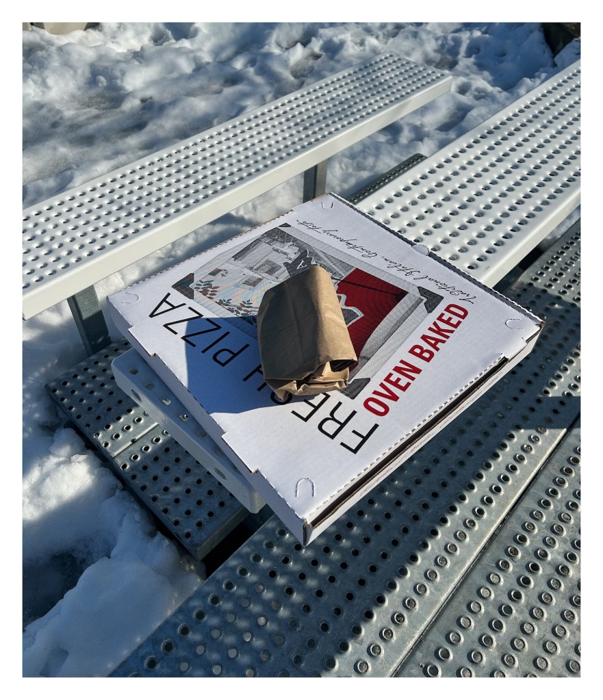 a pizze box rests on bleachers above snow-covered ground